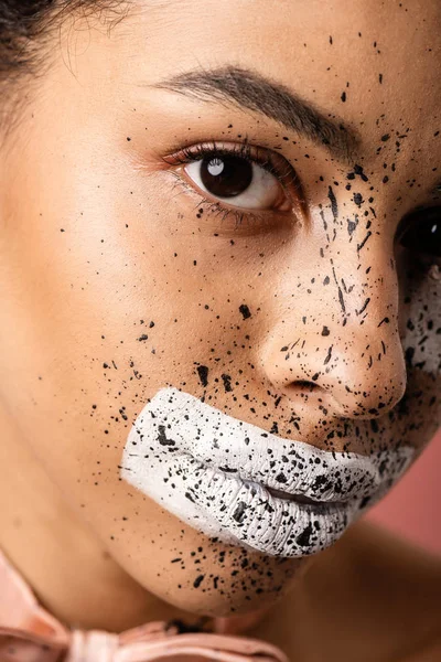 Vista de cerca de la hermosa mujer afroamericana con pajarita y pintura en la cara mirando a la cámara aislada en rosa - foto de stock