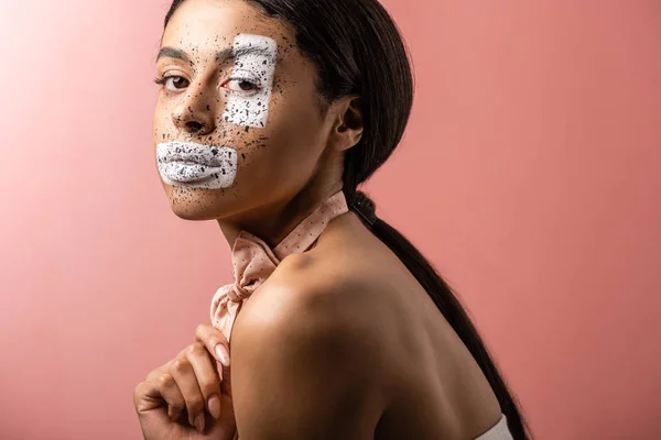 Bela menina americana africana com gravata borboleta e pintura no rosto olhando para a câmera isolada em rosa — Fotografia de Stock