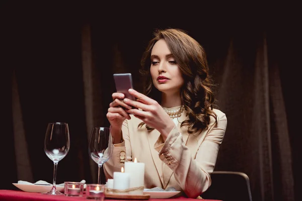Belle femme assise à table et utilisant smartphone dans le restaurant — Photo de stock
