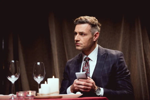 Handsome man in suit sitting at table and using smartphone in restaurant — Stock Photo