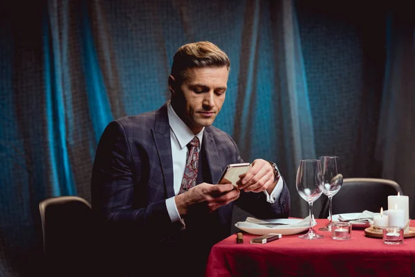 Bell'uomo in giacca e cravatta seduto a tavola e utilizzando lo smartphone nel ristorante — Foto stock