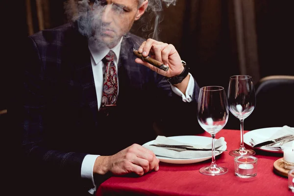 Mann im Anzug sitzt am Tisch und raucht Zigarre im Restaurant — Stockfoto