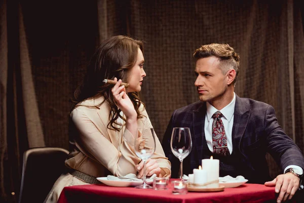Жінка сидить за столом і курить сигару, проводячи романтичну вечерю з красивим чоловіком в ресторані — стокове фото