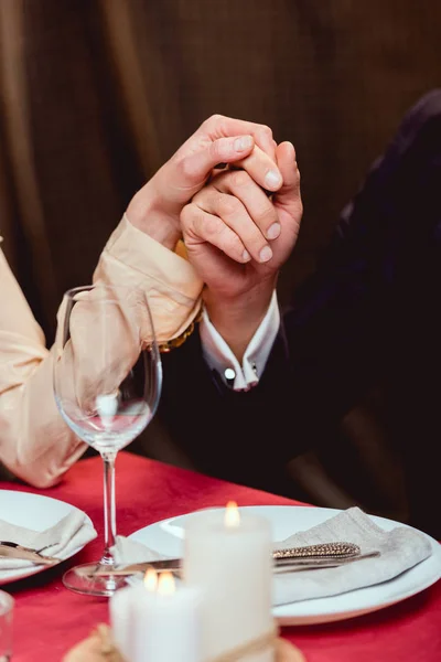 Vista cortada do casal de mãos dadas durante a data romântica no restaurante — Fotografia de Stock