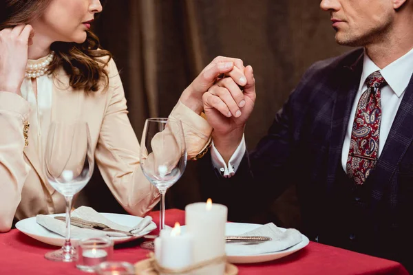 Cropped view of couple holding hands during romantic date in restaurant — Stock Photo