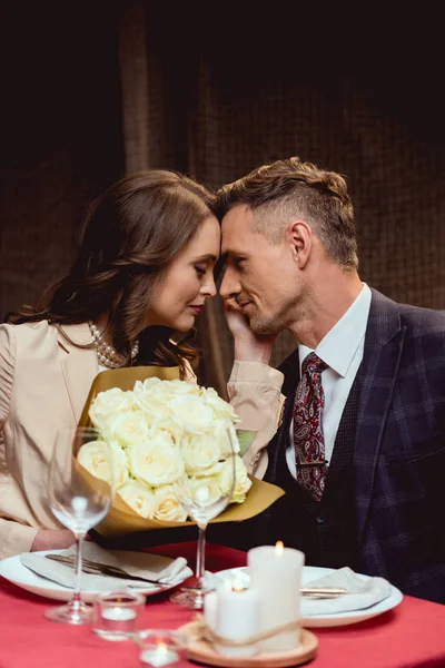 Bella coppia seduta a tavola con mazzo di fiori e guardarsi durante appuntamento romantico nel ristorante — Foto stock