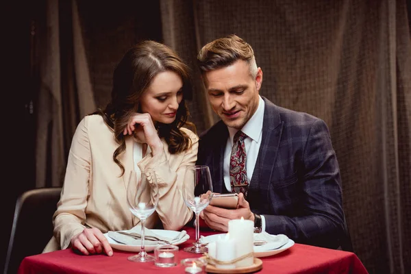 Pareja sentada en la mesa y el uso de teléfonos inteligentes durante la cita romántica en el restaurante - foto de stock