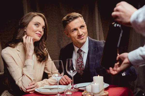 Garçom mostrando garrafa de vinho para belo casal durante data romântica no restaurante — Fotografia de Stock