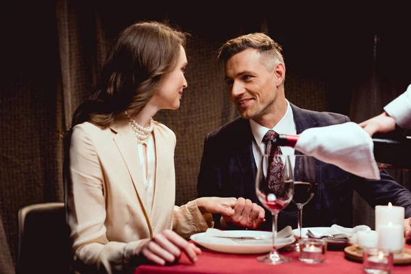 Camarero vertiendo vino tinto mientras pareja teniendo una cita romántica en restaurante - foto de stock