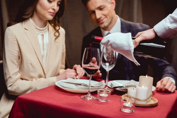 Camarero vertiendo vino tinto mientras pareja teniendo una cita romántica en restaurante - foto de stock