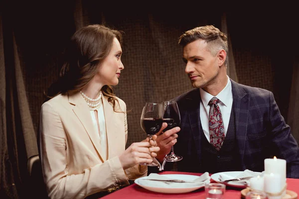 Casal sentado à mesa e copos clinking de vinho tinto durante a data romântica no restaurante — Fotografia de Stock