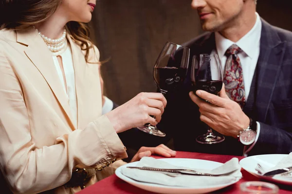Vista parcial de pareja tintineo vasos de vino tinto durante la cita romántica en el restaurante — Stock Photo