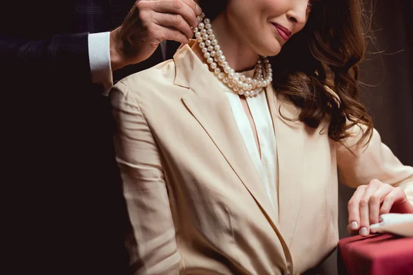 Vista recortada del hombre poniendo collar de perlas en la mujer sonriente - foto de stock