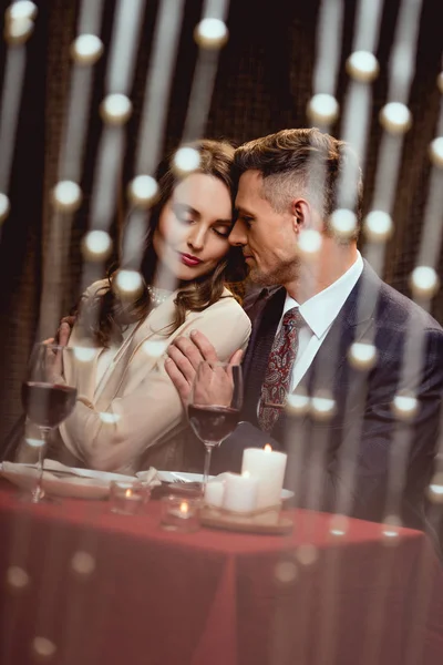 Man gently embracing woman during romantic date in restaurant with bokeh lights on foreground — Stock Photo