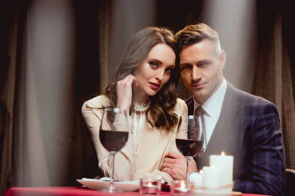 Selective focus of beautiful couple with glasses of red wine looking at camera during romantic date in restaurant — Stock Photo