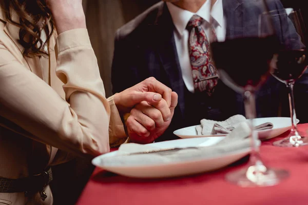 Partial view of couple holding hands while having romantic date in restaurant — Stock Photo