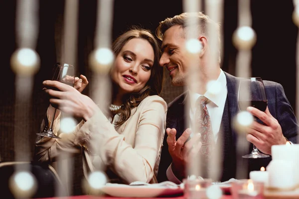 Beautiful smiling couple holding glasses of red wine and talking during romantic date in restaurant — Stock Photo