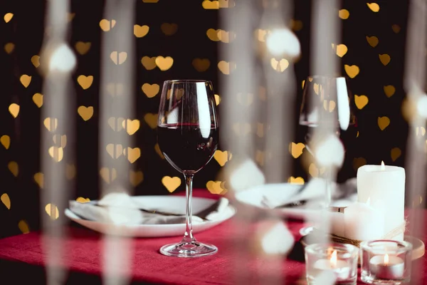 Selective focus of red wine glasses with heart shaped bokeh on background — Stock Photo