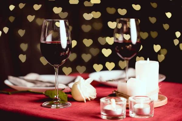 Enfoque selectivo de copas de vino tinto con bokeh en forma de corazón y ajuste de mesa en el fondo - foto de stock