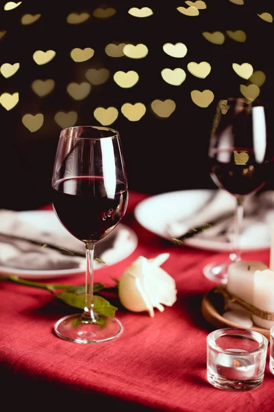Fuoco selettivo di bicchieri di vino rosso con bokeh a forma di cuore e tavola impostazione su sfondo — Foto stock