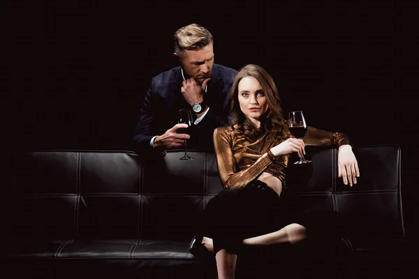 Handsome man looking at beautiful woman with glass of red wine isolated on black — Stock Photo