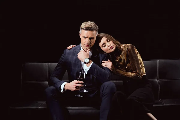 Schöne Frau sitzt auf der Couch und umarmt gutaussehenden Mann mit einem Glas Rotwein isoliert auf schwarz — Stockfoto