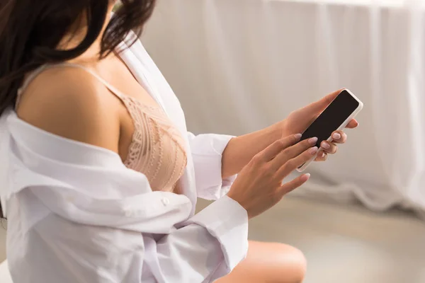 Vista recortada de la mujer en camisa blanca usando teléfono inteligente con pantalla en blanco - foto de stock