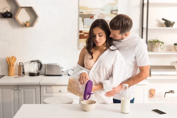 Beau jeune couple câlin tout en prenant le petit déjeuner à la maison — Photo de stock