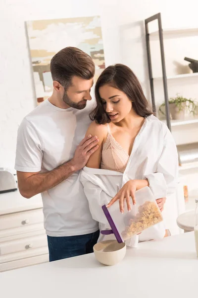 Bonito jovem casal abraçando enquanto toma café da manhã em casa — Fotografia de Stock