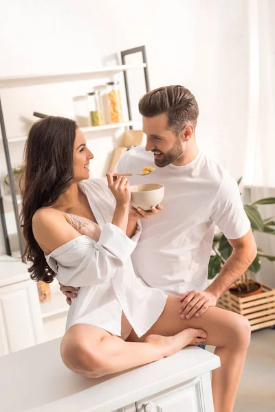 Smiling woman feeding man with cereal during breakfast in morning — Stock Photo