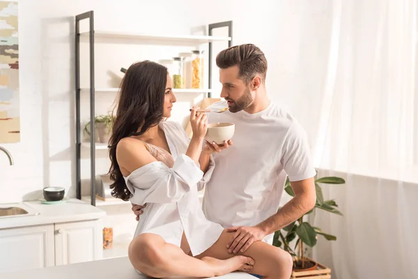 Smiling woman feeding man with cereal during breakfast in morning — Stock Photo