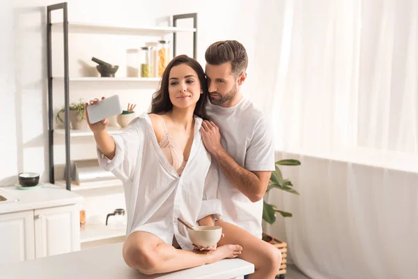 Joven pareja tomando selfie en smartphone mientras desayuna en casa - foto de stock