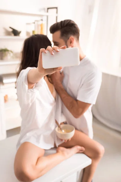 Пара в белой одежде делает селфи на смартфоне дома во время завтрака — стоковое фото