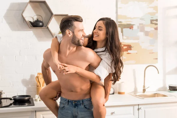 Bel homme torse nu donnant tour de dos à la femme souriante dans la cuisine — Photo de stock
