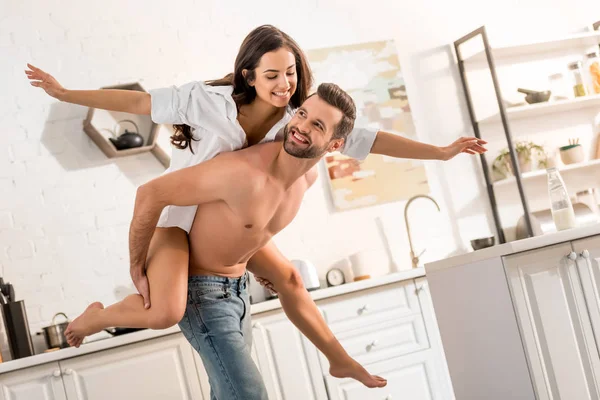 Красивый мужчина без рубашки катает на спине красивую женщину на кухне — стоковое фото