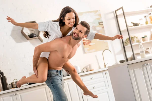 Hombre sin camisa guapo dando paseo a cuestas a la hermosa mujer en la cocina - foto de stock