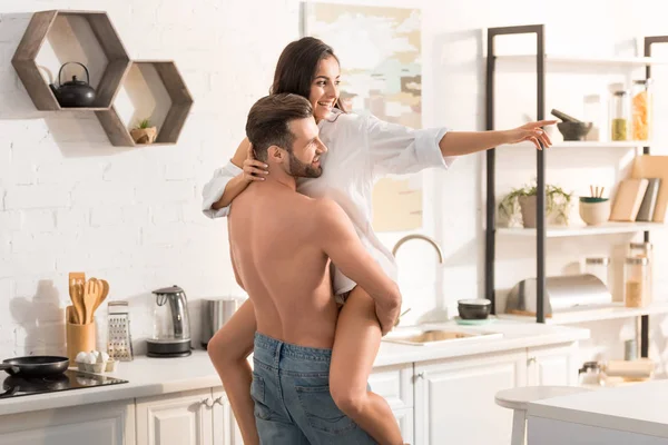 Enfoque selectivo del hombre sin camisa abrazando a la mujer sonriente en la cocina - foto de stock