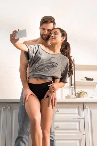 Young sexy couple hugging and taking selfie on smartphone in kitchen — Stock Photo