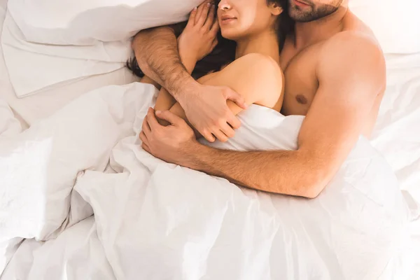 Cropped view of nude couple embracing while sleeping in bed — Stock Photo