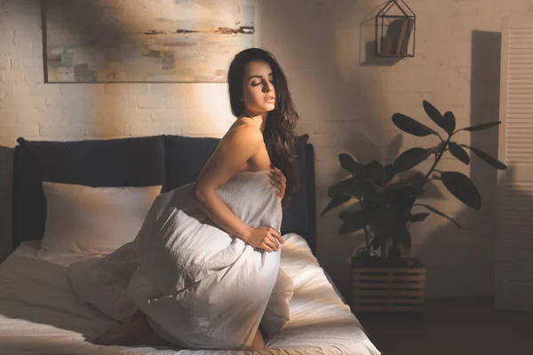 Bela mulher sensual cobrindo corpo com edredão e sentado na cama em casa — Fotografia de Stock