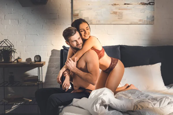 Schöne lächelnde Frau umarmt hemdlosen Mann auf dem Bett zu Hause — Stockfoto