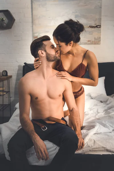 Mujer seductora en lencería abrazando al hombre sin camisa en la cama — Stock Photo