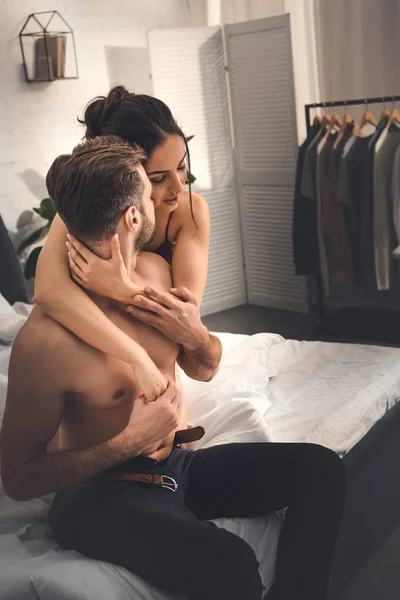 Selective focus of beautiful woman embracing shirtless man on bed at home — Stock Photo