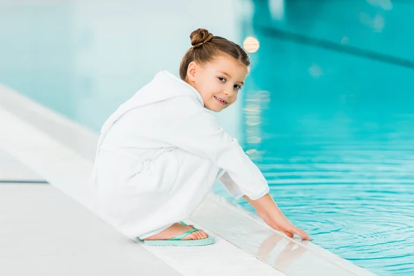 Enfant gai en peignoir touchant l'eau dans la piscine — Photo de stock