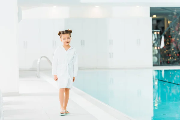 Cheerful kid in bathrobe walking near swimming pool — Stock Photo