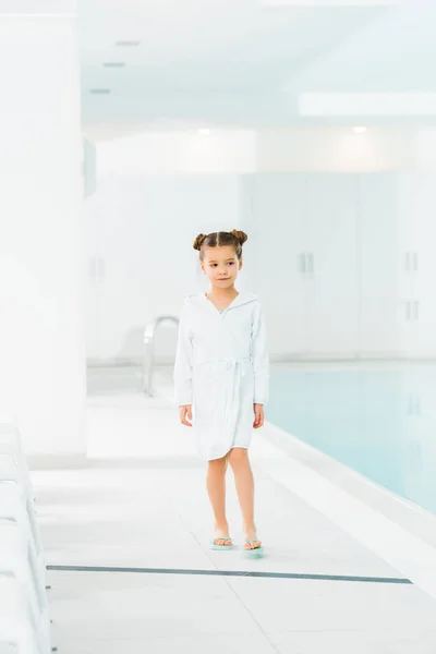 Mignon enfant en peignoir marchant près de la piscine — Photo de stock