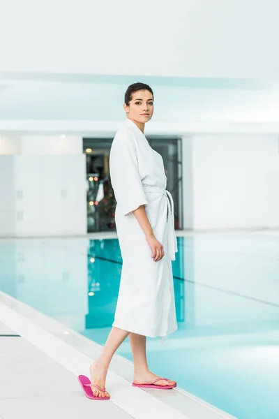 Attractive woman in bathrobe standing near swimming pool — Stock Photo