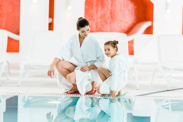 Felice madre in accappatoio guardando la figlia vicino alla piscina — Foto stock