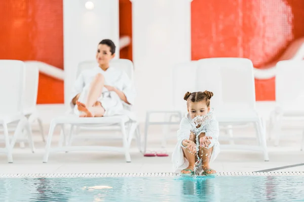 Selective focus of cute kid playing with water near mother on deck chair — Stock Photo