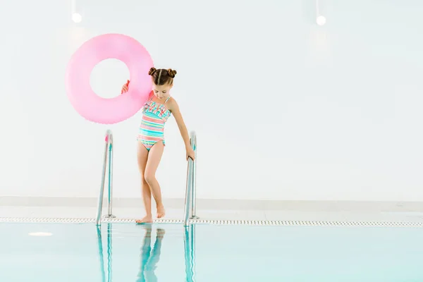 Adorable kid standing near swimming pool and holding inflatable ring — Stock Photo